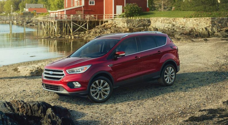 A red 2017 Ford Escape is shown parked on dirt next to a small pond.