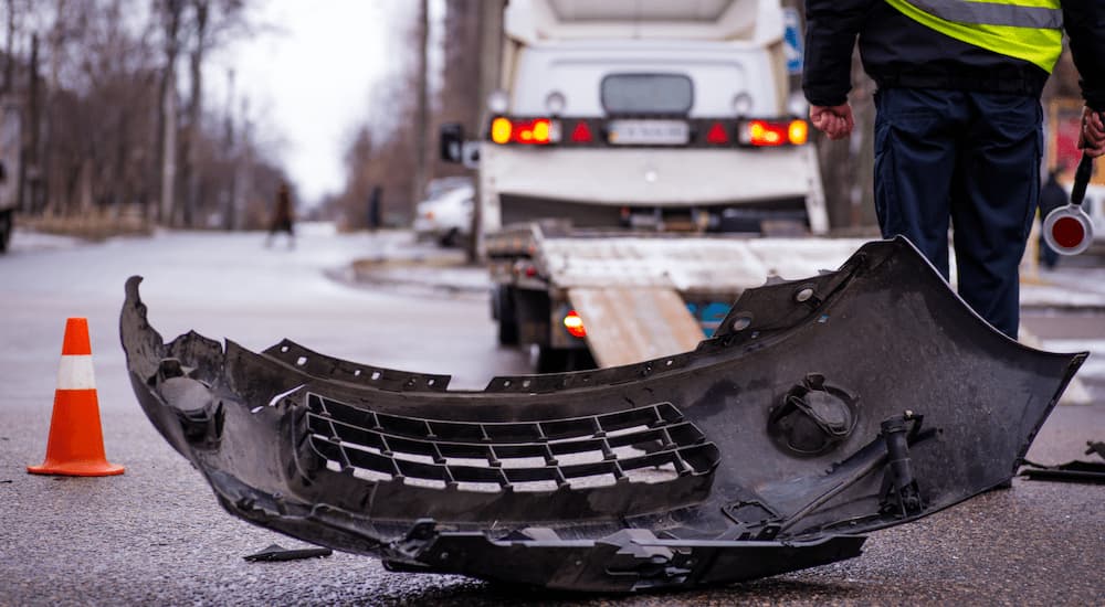 A car bumper is shown laying on the ground near a tow truck.