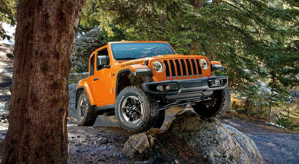 An orange 2019 Jeep Wrangler Rubicon is shown from the front while driving over a rock.