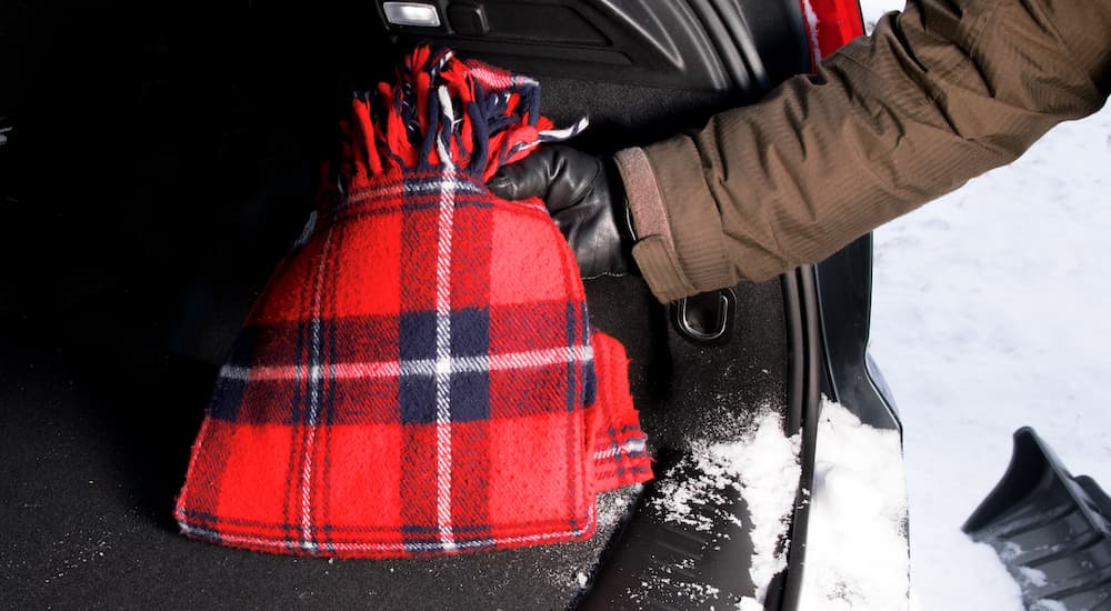 A gloved hand is shown stowing a blanket in the trunk of a car.