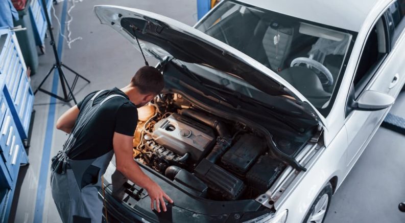 A mechanic is shown inspecting the engine in a silver vehicle.