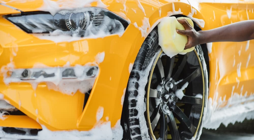 A person is shown washing a yellow Ford Mustang.