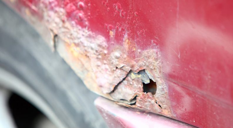 A rust hole is shown on a red vehicle.