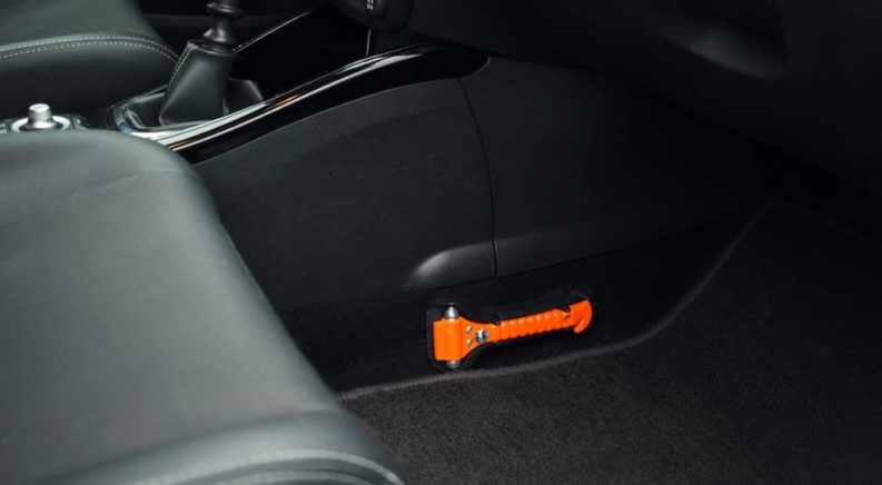 An orange seat belt cutter and window breaker is shown in a foot well.
