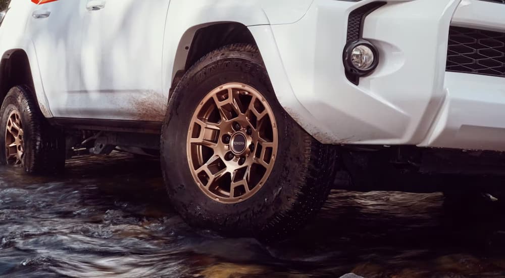 A close up of the tire on a white 2023 Toyota 4Runner 40th Anniversary Edition while driving through a river.