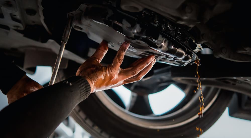 A close up of a mechanic checking the transmission fluid underneath a vehicle.