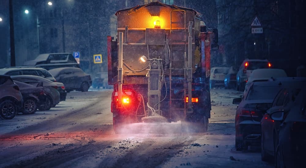 A truck is shown from the rear salting a road during winter.