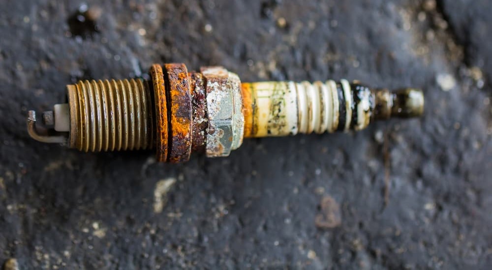 A dirty and damaged spark plug is shown on the ground.