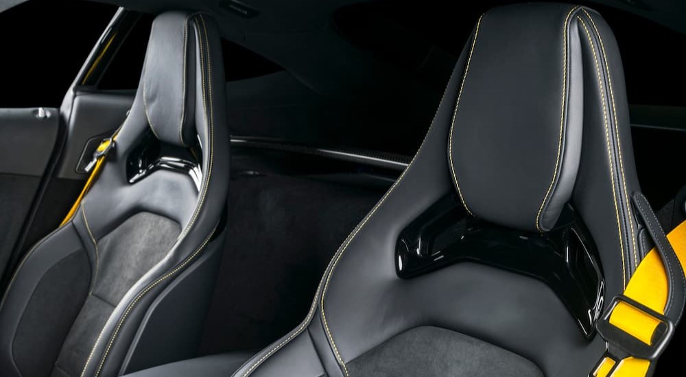 Two black race seats are shown with yellow seat belts inside of a vehicle.