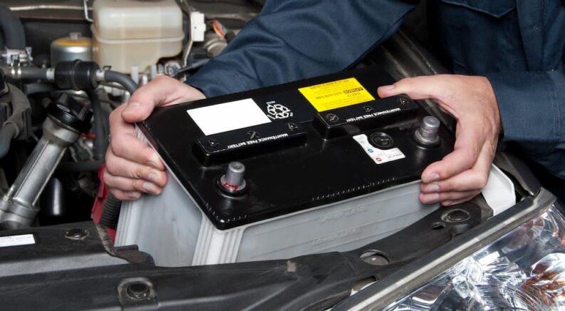 A mechanic is shown replacing a battery in a vehicle.