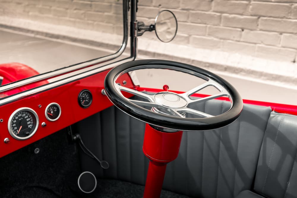 A black and chrome aftermarket steering wheel is shown inside of a red classic car.
