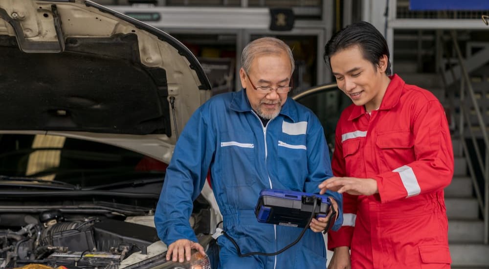 Two mechanics are shown using an OBD2 scanner.