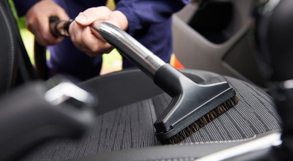 A person is shown vacuuming a seat of a car.