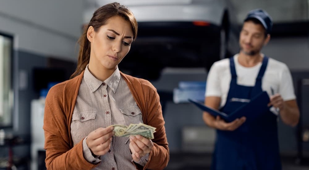 A person is shown counting money for a vehicle repair bill.