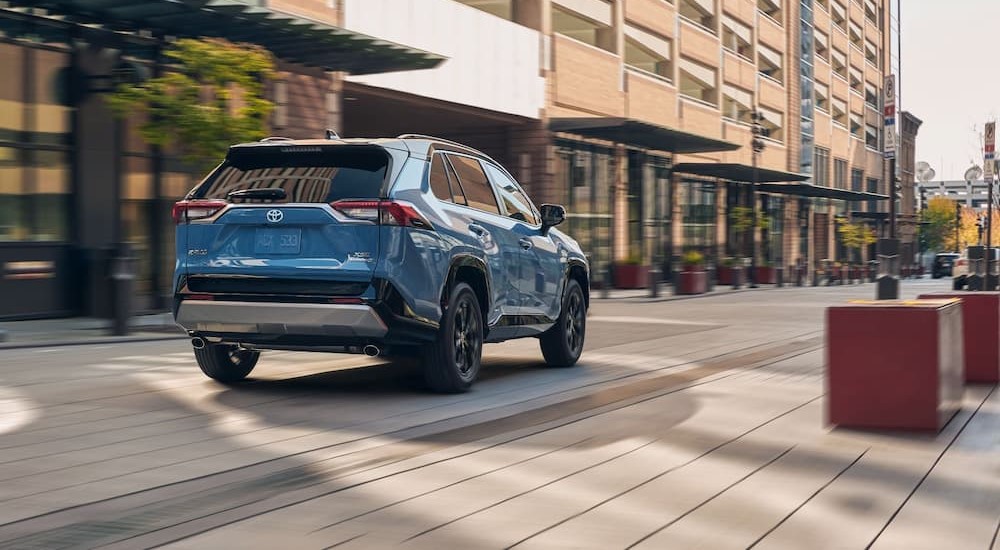 A blue 2024 Toyota RAV4 Hybrid is shown driving in a city.