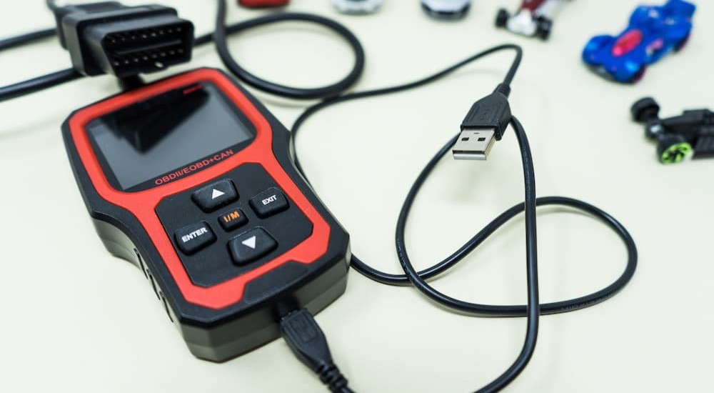 A black and red OBDII reader is shown near toy cars.