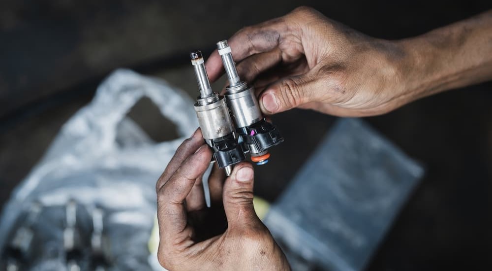 A person is shown holding and comparing a clean and dirty fuel injector.