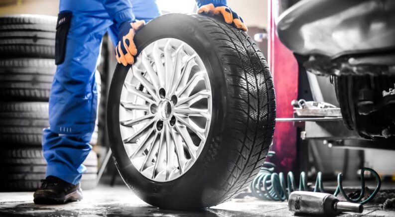 A mechanic is shown rolling a wheel in a garage.