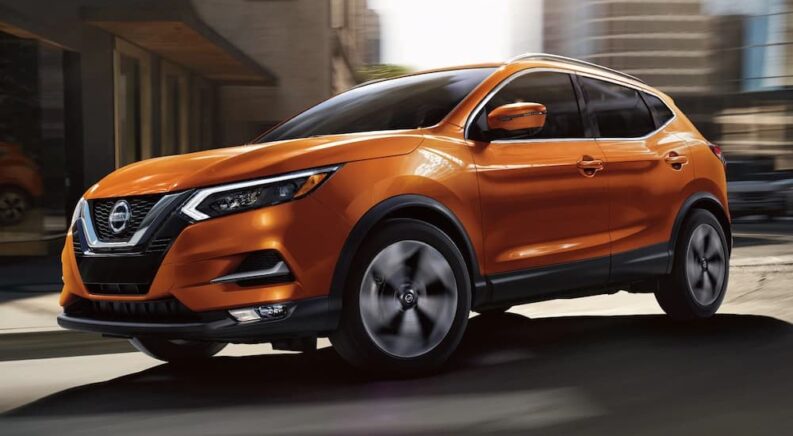 An orange 2022 Nissan Rogue is shown driving to a Nissan dealer.