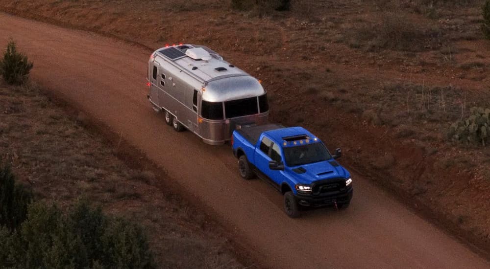 A blue 2024 Ram 2500 is shown towing a trailer on a dirt road.