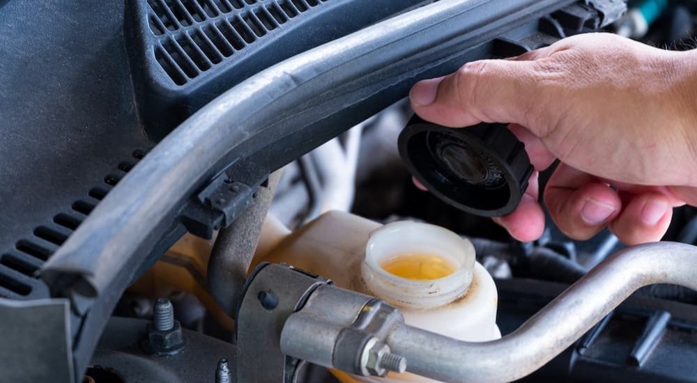 A mechanic is shown holding a black cap and checking fluid levels in a vehicle.