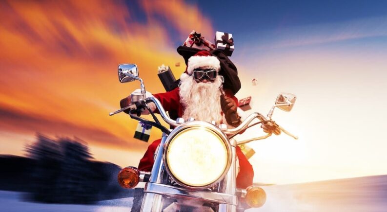 Santa is shown riding a motorcycle and holding presents.