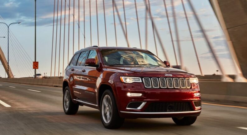 One of many popular used cars, a burgundy 2020 Jeep Grand Cherokee, is shown driving on a bridge.