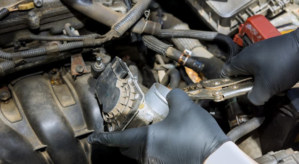 Close up of hands removing a throttle body from a dusty engine.