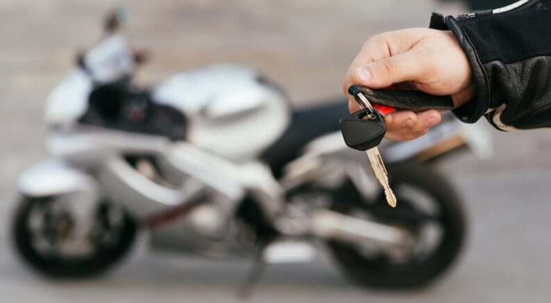 A person is shown holding a key at a used motorcycle dealer.
