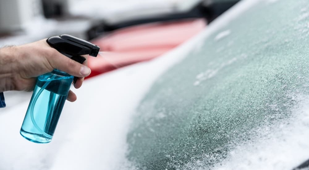 A person is shown spraying de-icer onto a frozen windshield.