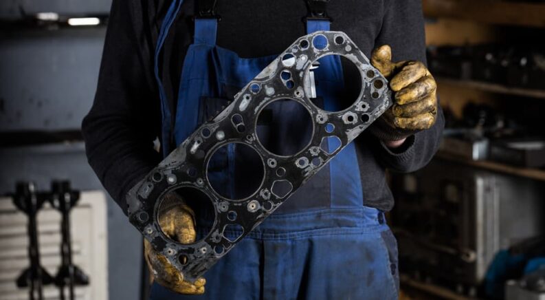 A mechanic is shown holding a head gasket during an engine repair.