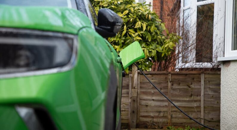 Closeup of a green PHEV charging outside a home.