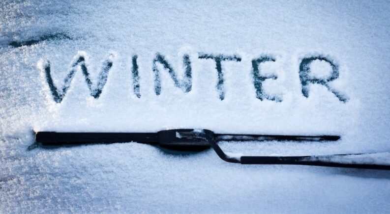 Winter is shown written o a snowy windshield.