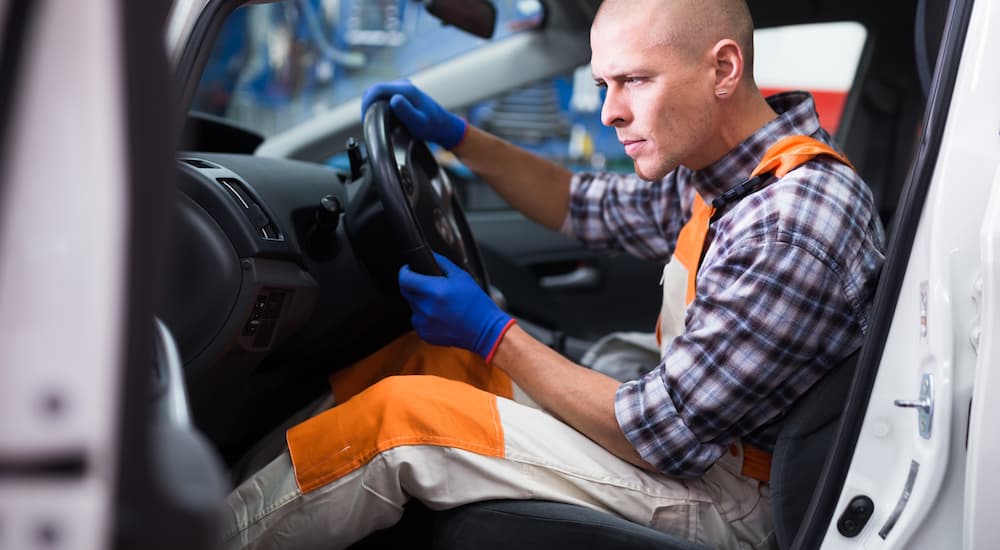 A mechanic working on a car's steering wheel from the driver's seat.