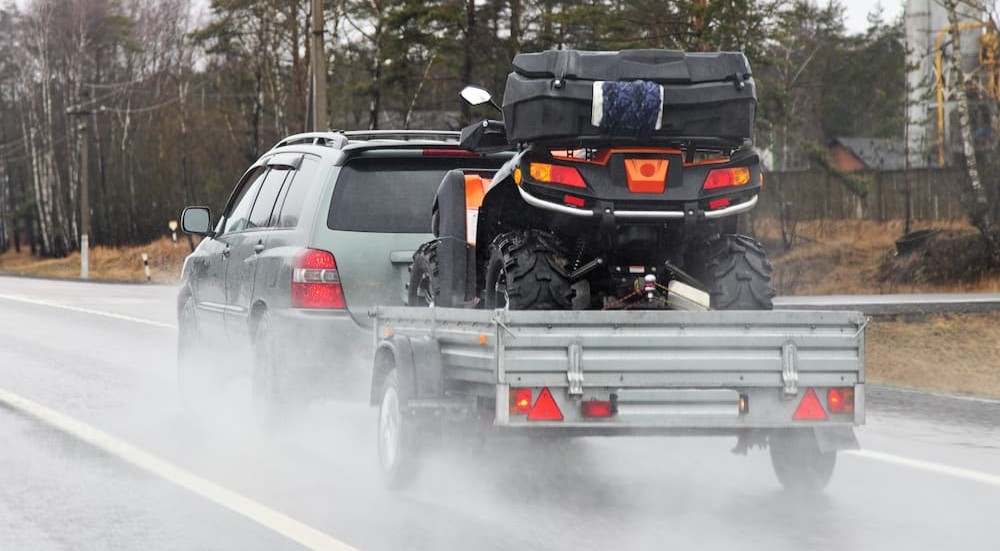 A silver vehicle is shown using a trailer to tow an ATV.