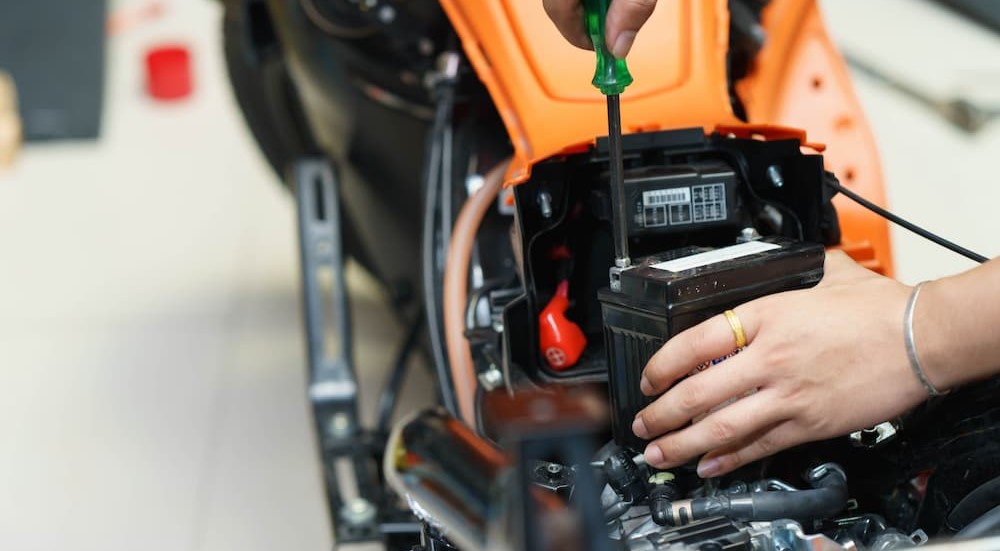 A person is shown replacing a battery in a motorcycle.