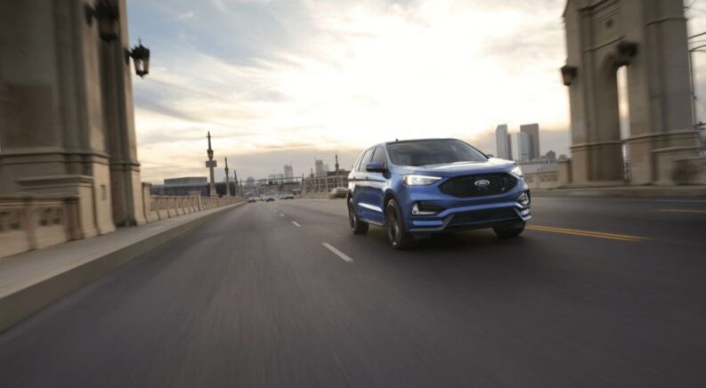 A popular used Ford Edge for sale, blue 2021 Ford Edge, is shown driving on a bridge.