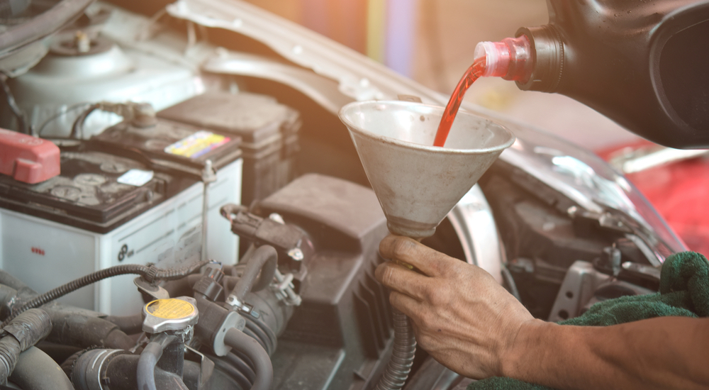 A mechanic is shown pouring transmission fluid through a funnel into an engine.