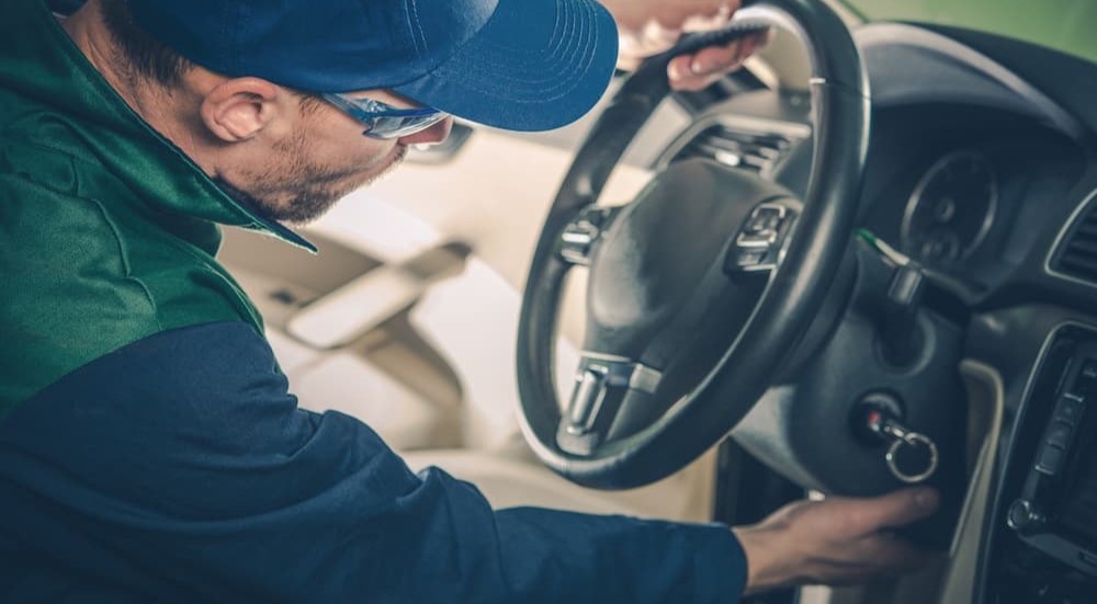A mechanic is shown checking under the steering wheel.