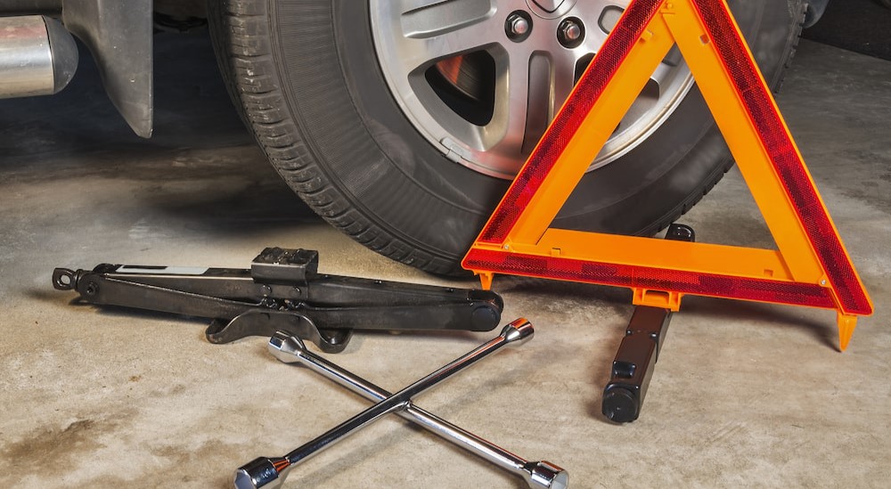 A jack, lug wrench and safety triangle are shown near a wheel.