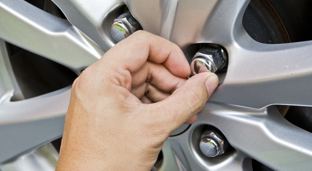 A hand is shown touching a lug nut on a wheel.