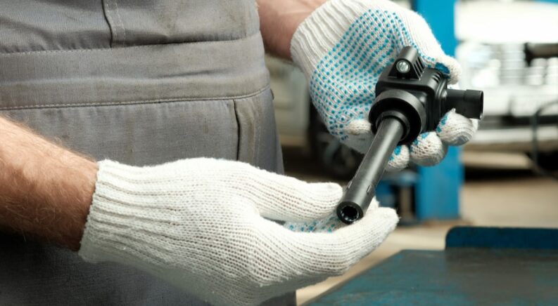 A mechanic is shown holding an ignition coil at an auto repair shop.
