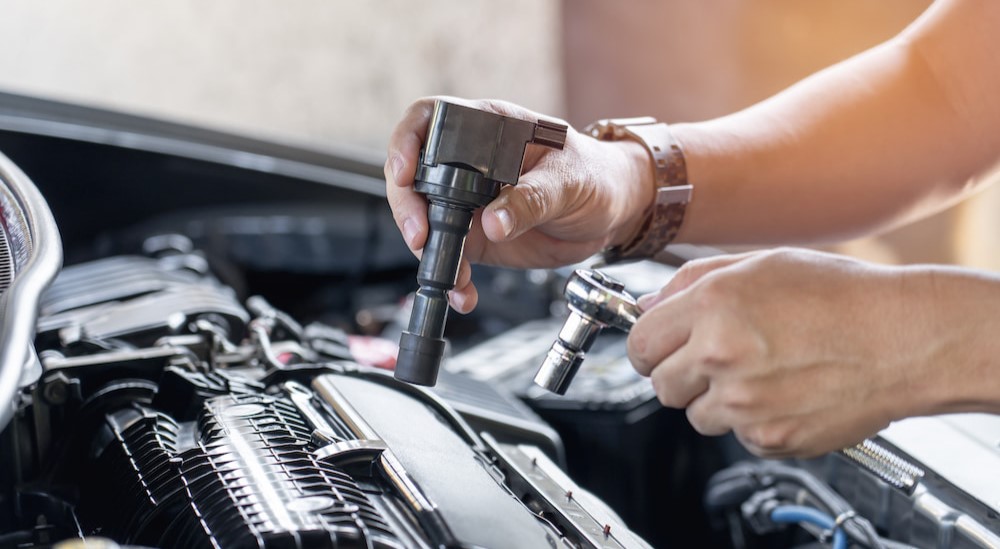 A mechanic is shown replacing an ignition coil in an engine.