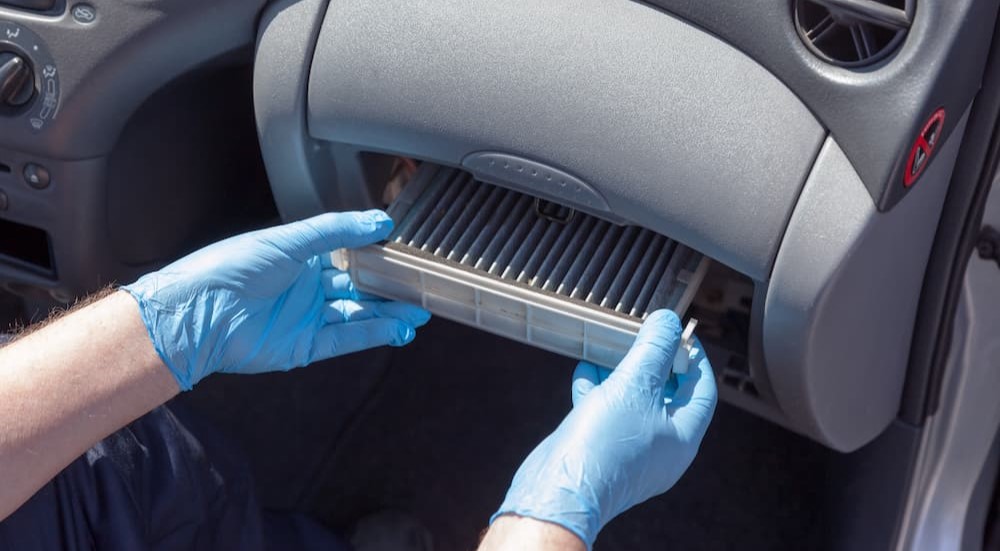 A mechanic is shown removing a dirty air filter from a glove compartment. 