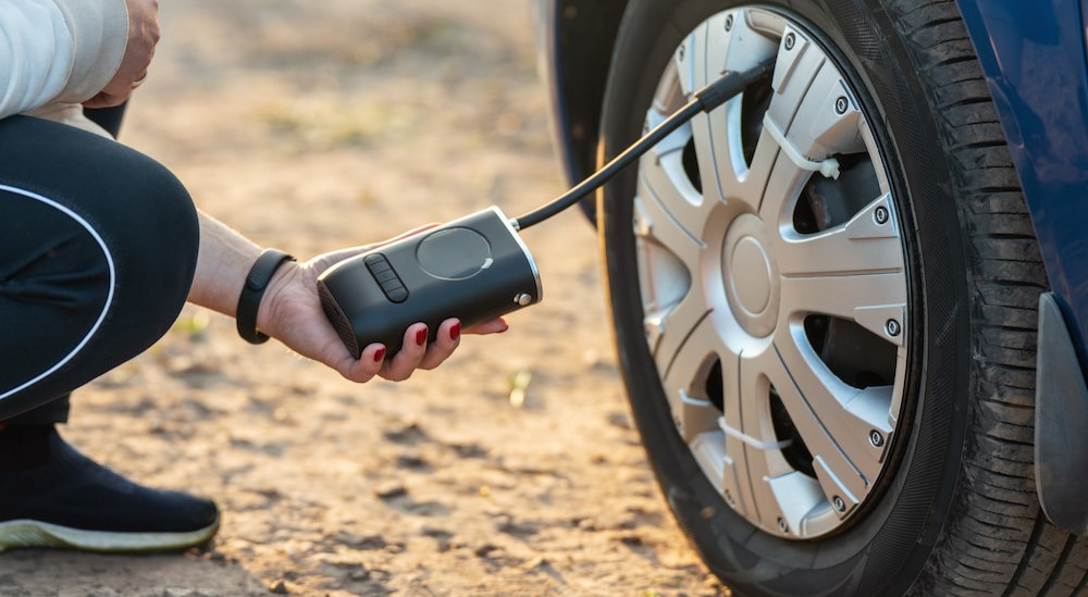 A person is shown using a handheld portable tire inflater.