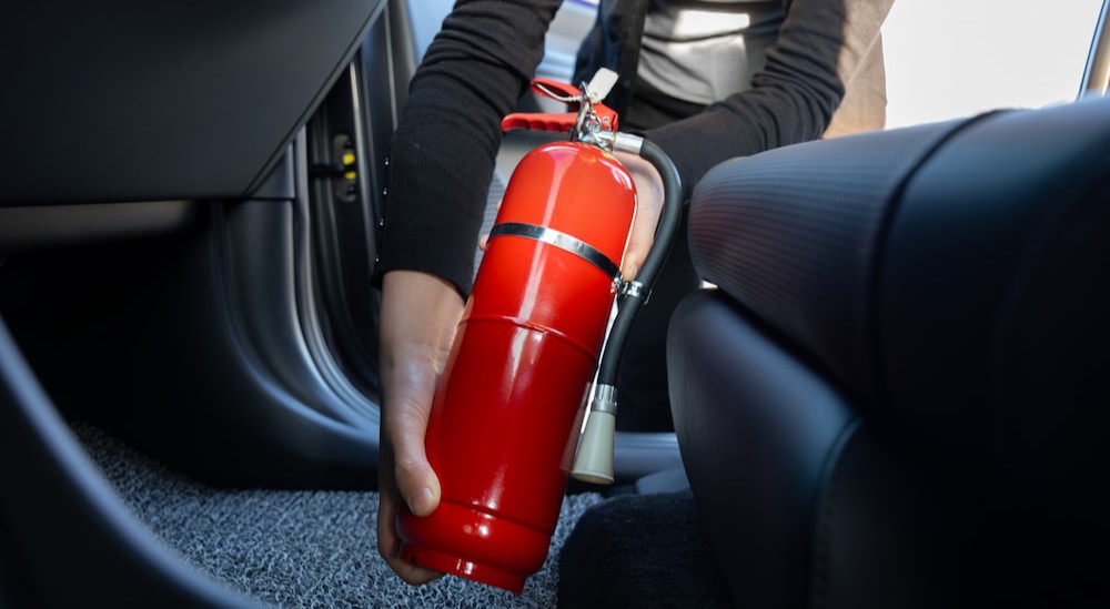 A person is shown holding a red fire extinguisher in a vehicle.