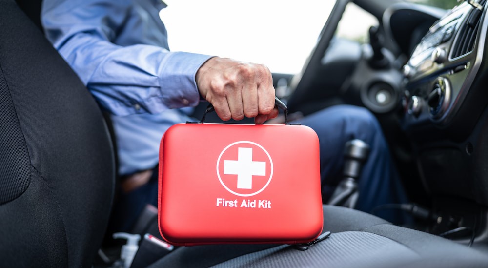 A person is shown holding a first aid kit in a vehicle.