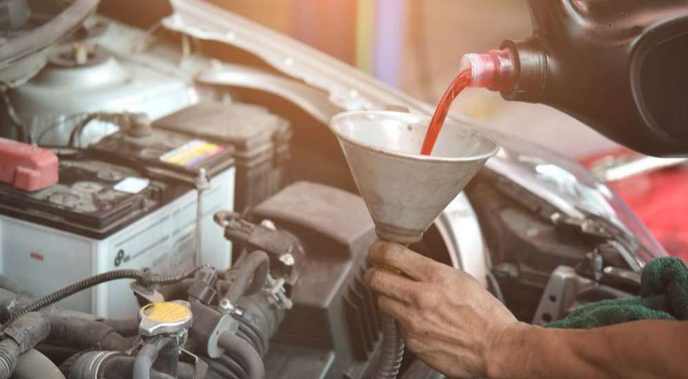 A mechanic is shown pouring transmission fluid into a funnel.