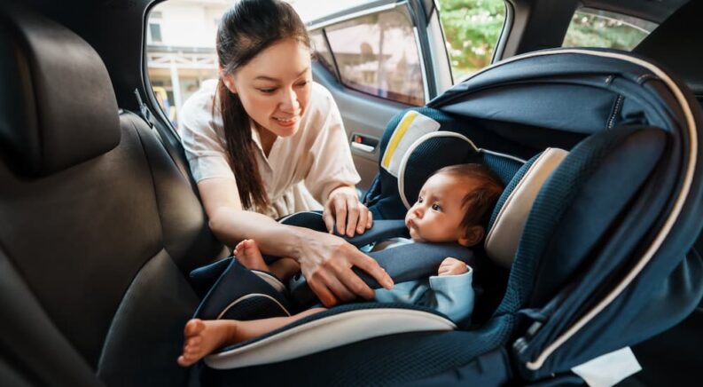 A mom is buckling a baby into a carseat.