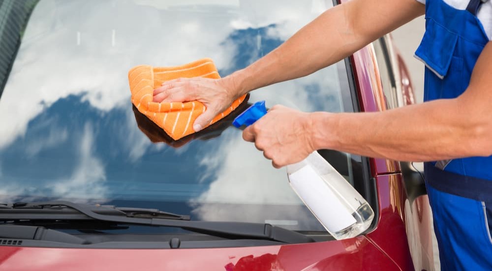 A person is shown spraying a windshield and wiping it with an orange cloth. 